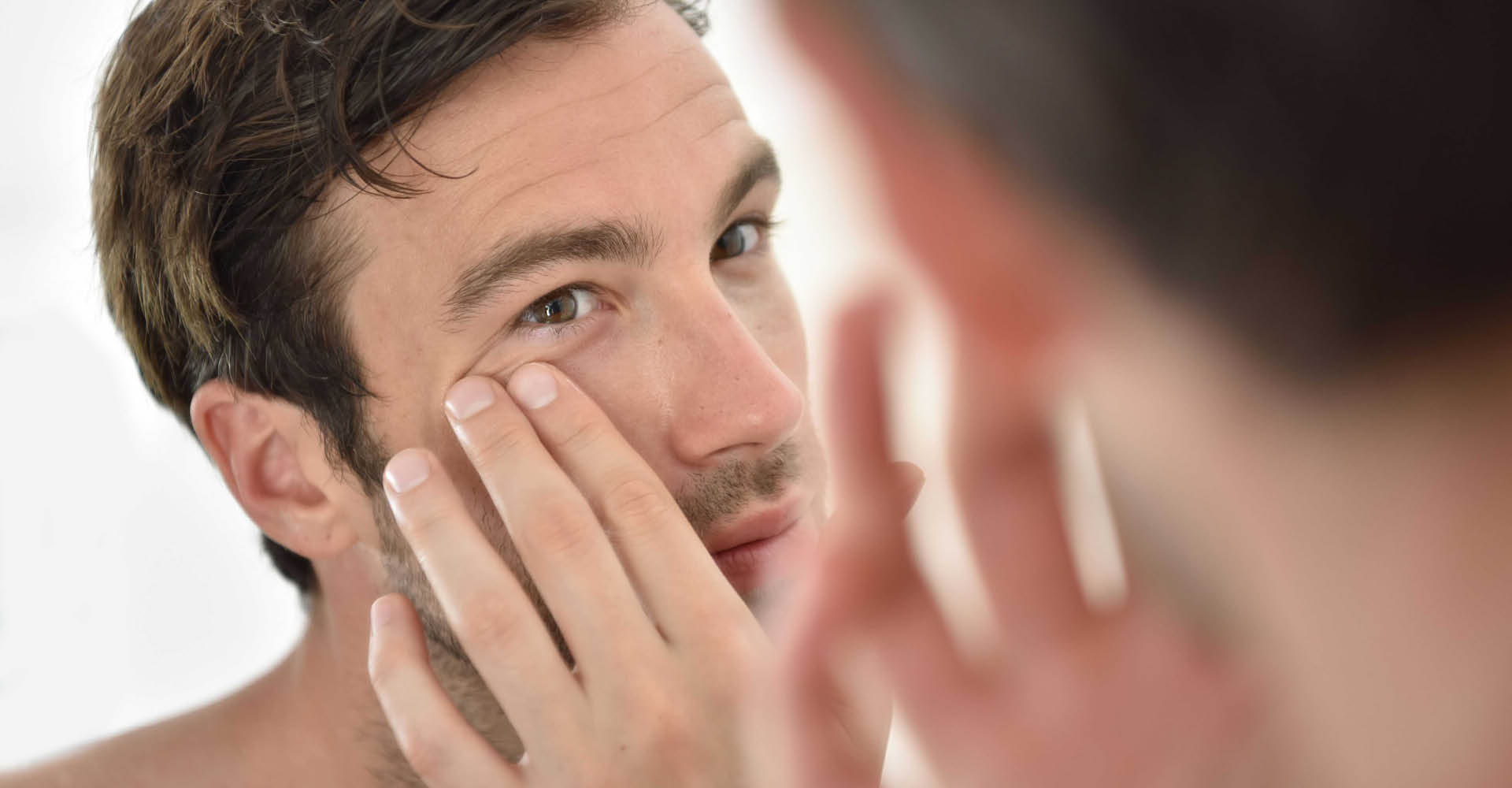 Immagine di un uomo che si sta guardando allo specchio e con una mano si sta toccando l'occhio
